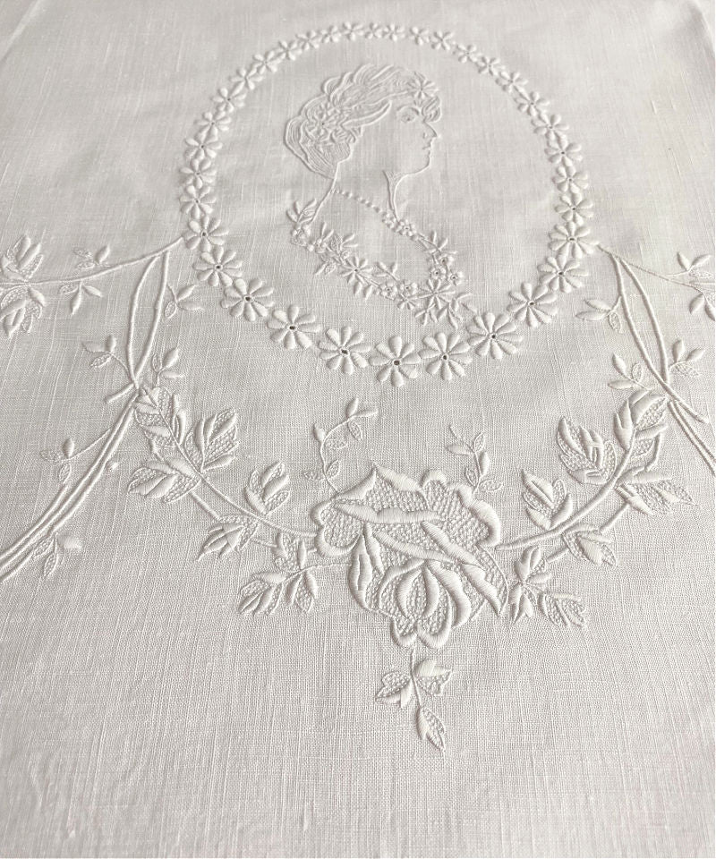 Close-up of white Appenzellembroidered hand towel with a portrait and floral design, showing detailed flower patterns and a monogram.