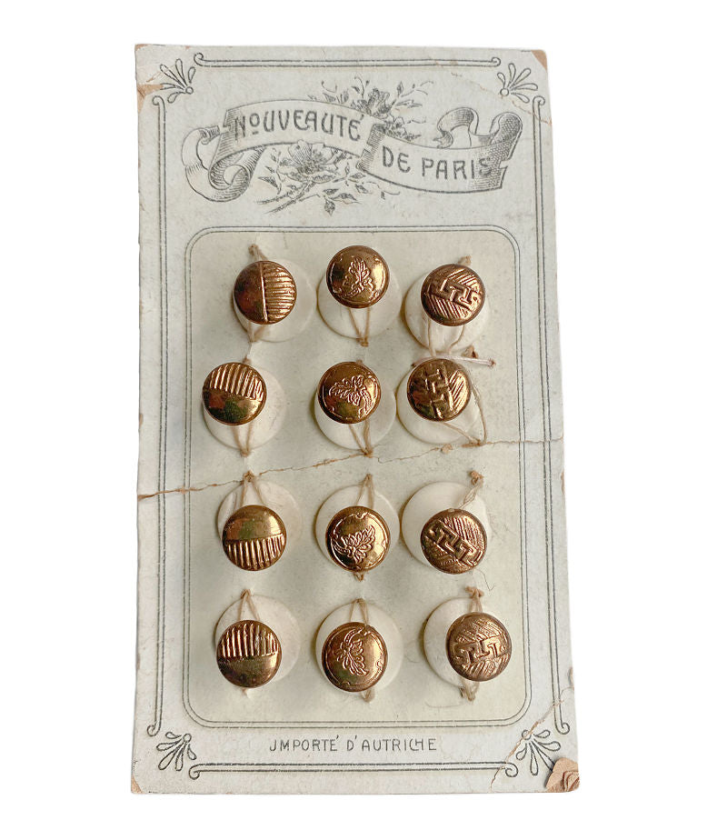 A collection of twelve antique French gold and cream cufflinks and collar buttons displayed on an original card with 'Nouveaute de Paris' printed on it.