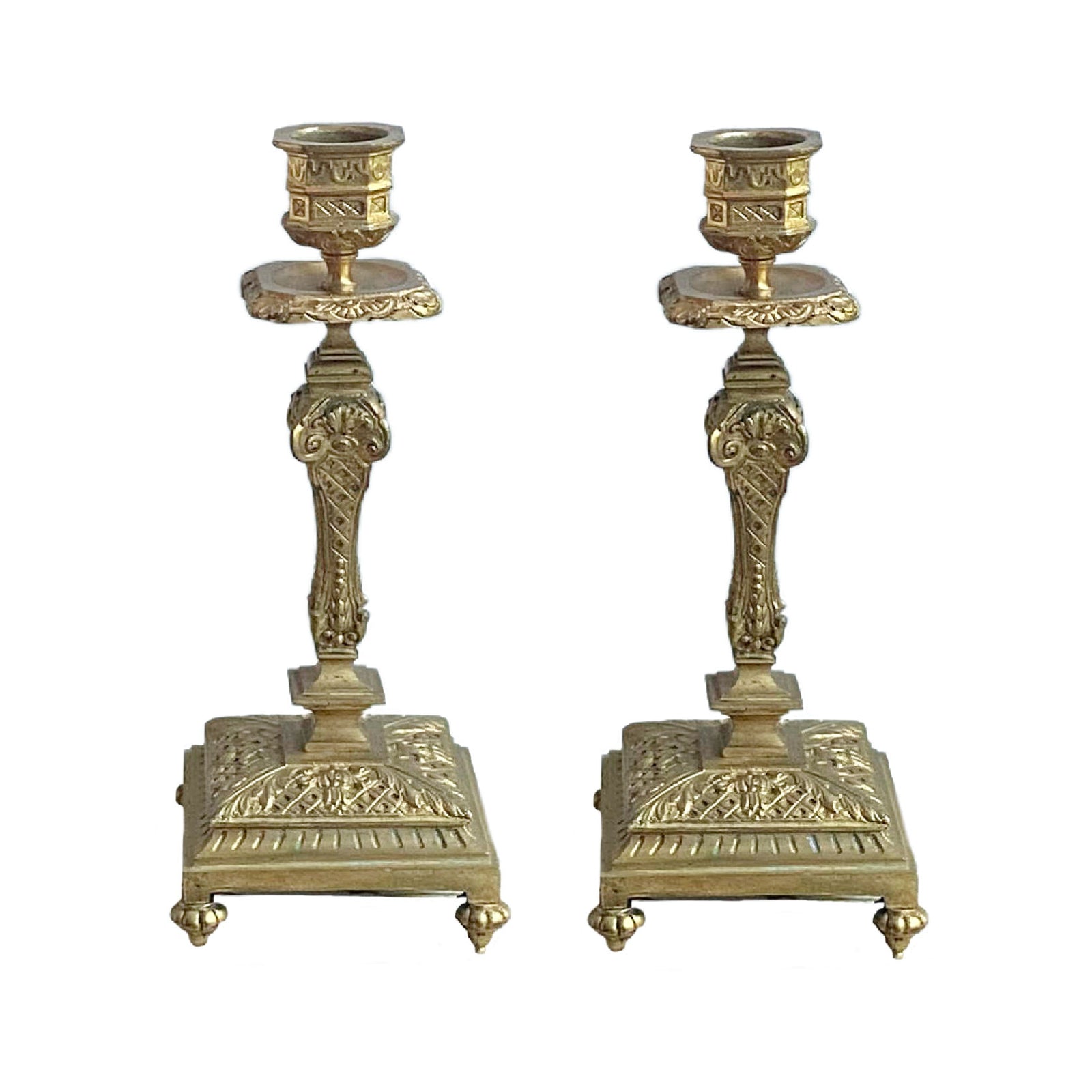 A pair of antique gilt brass candlesticks with French Empire style decoration on a white background.