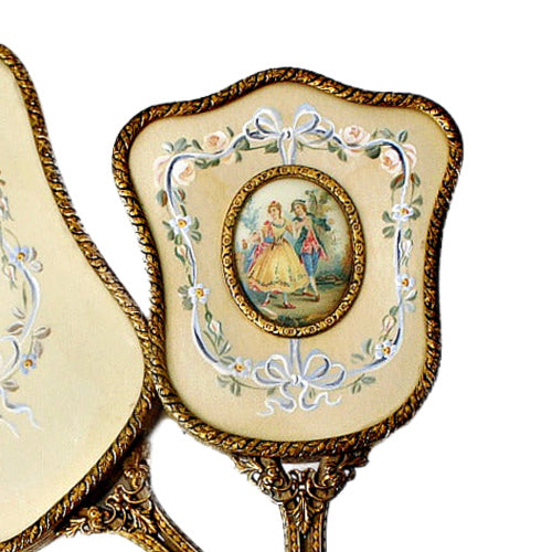 Exquisite hand-painted vanity mirror and brush set with gilt filigree and romantic courting scenes. A rare and elegant treasure for the antique dressing table.