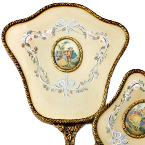 Exquisite hand-painted vanity mirror and brush set with gilt filigree and romantic courting scenes. A rare and elegant treasure for the antique dressing table.