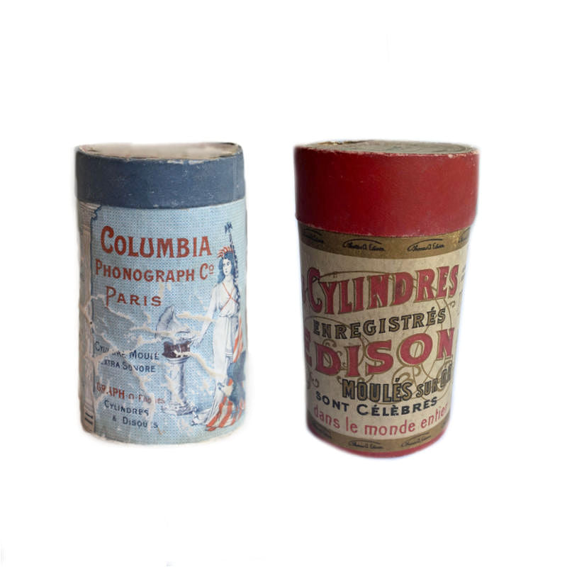 Two antique French phonograph cylinders in original boxes, one labeled Columbia and the other labeled Edison, with decorative designs and branding.