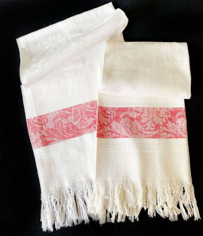 A pair of antique damask linen white and red hand towels with fringes and a foliate design woven in the fabric.