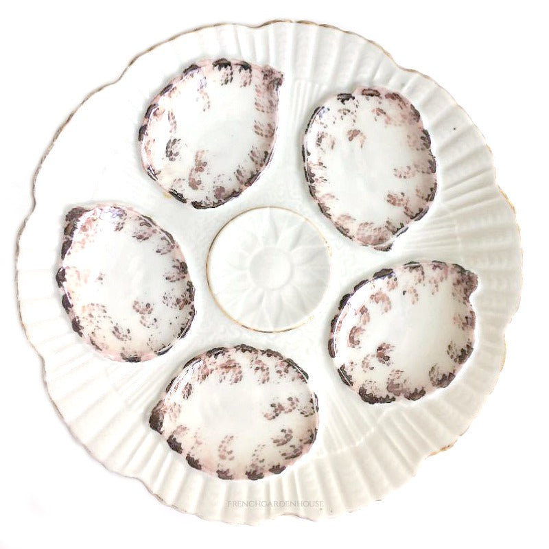 An antique porcelain oyster plate with purple luster details, featuring five wells for oysters and a central spiral well for lemon or butter.