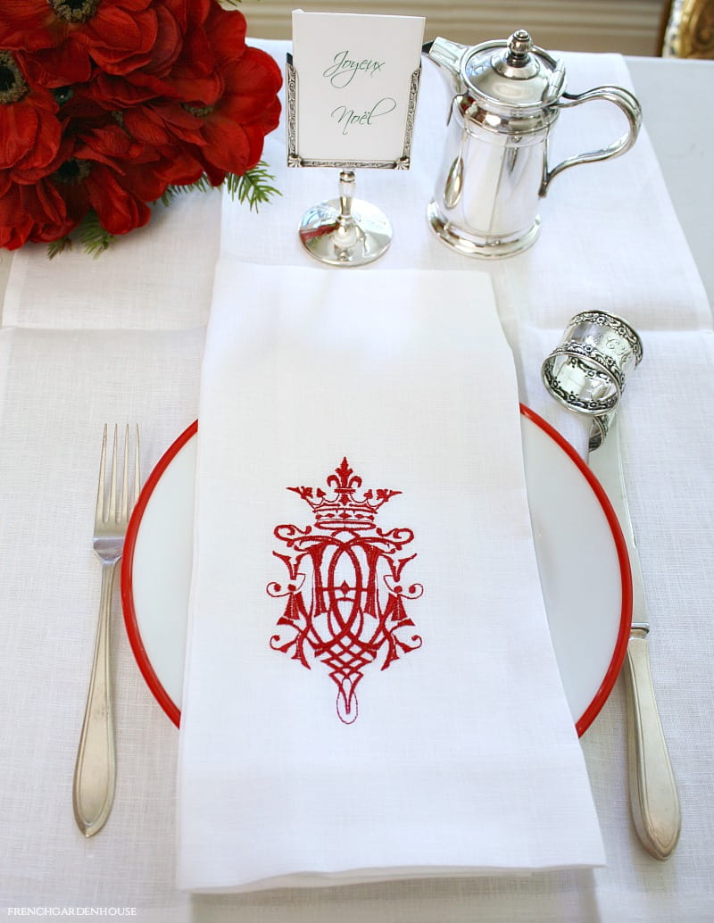 A white and red embroidered towel with a royal crest, laid out on a white plate with a hotel silver teapot and silverware in the background.