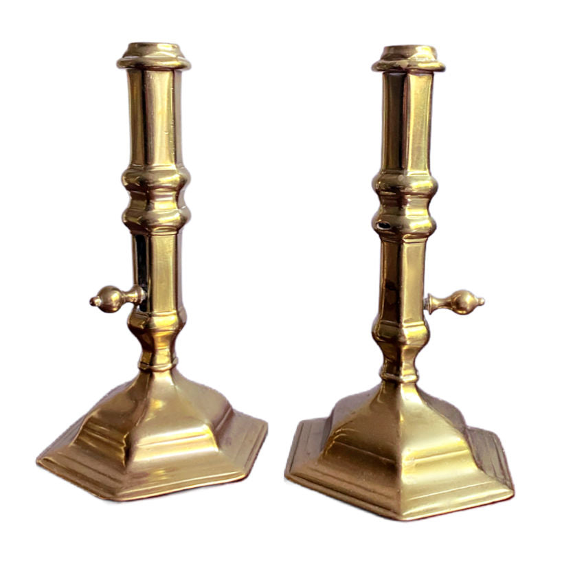A pair of antique brass side-eject candlesticks with six-sided flared bases and central columns, featuring side buttons for ejecting candle stubs.