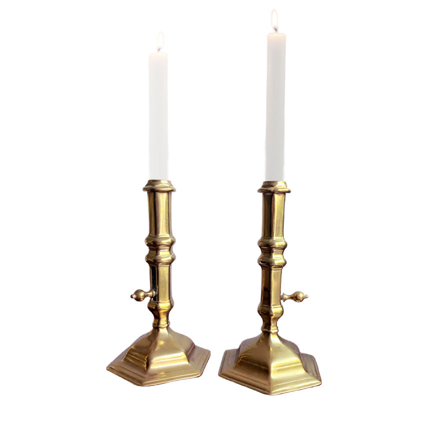 A pair of antique brass side-eject candlesticks with six-sided flared bases and central columns, featuring side buttons for ejecting candle stubs.