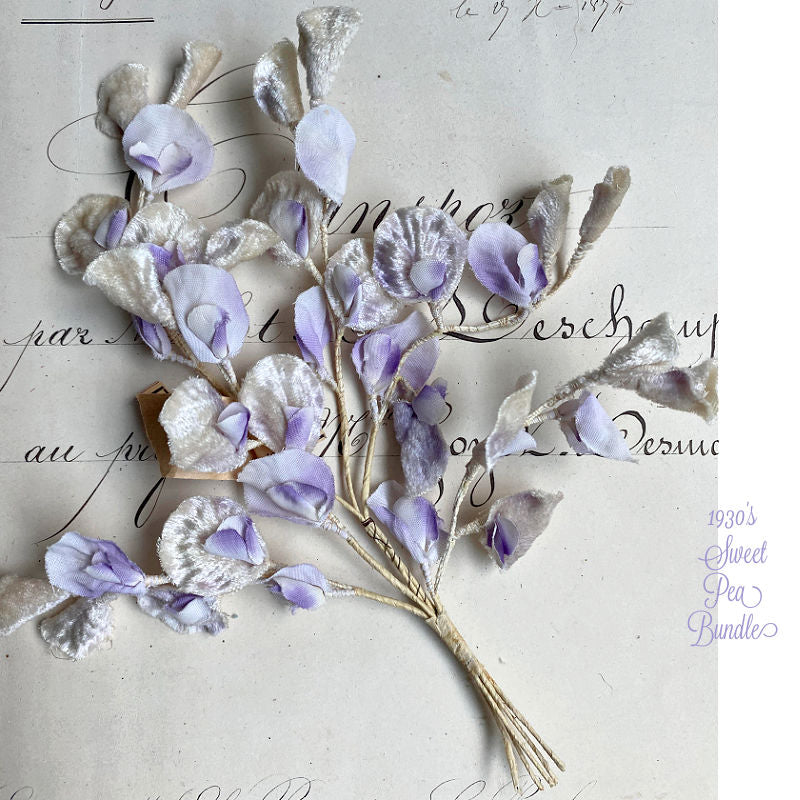 A bundle of antique French silk and velvet lavender sweet pea spray placed on an antique French written document background.