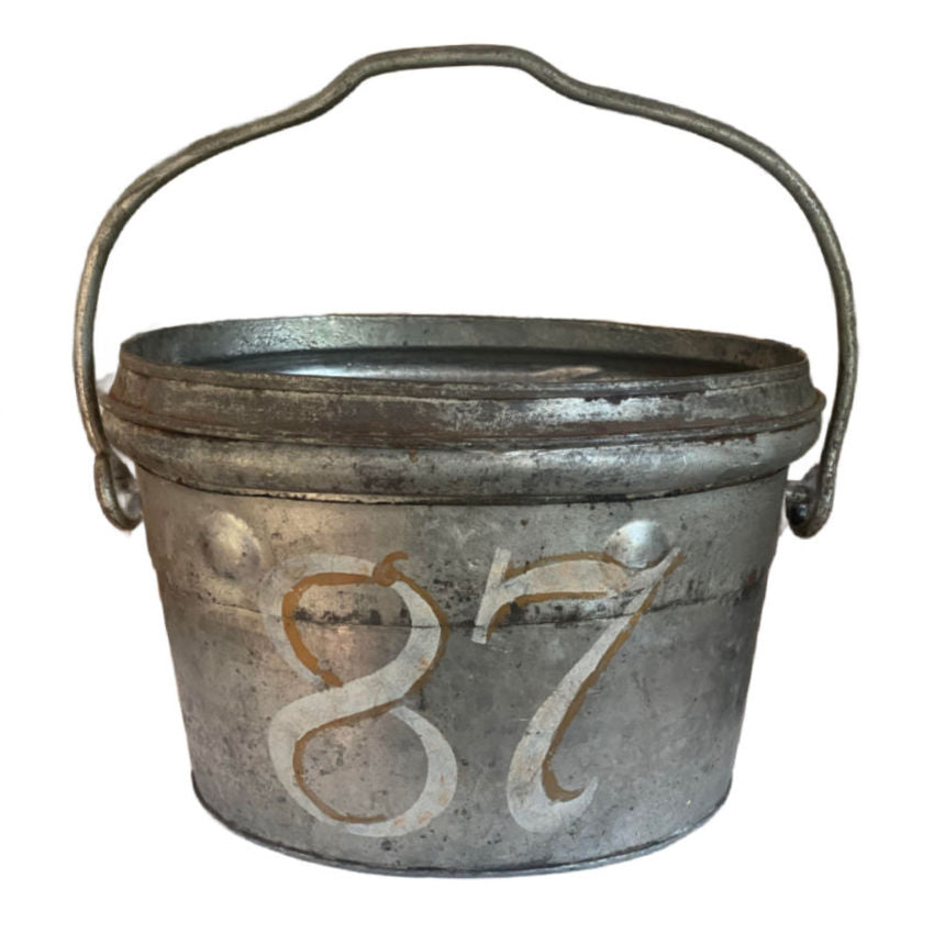 An antique  firefighter's bucket with a patina finish and the number 87 painted on the side.