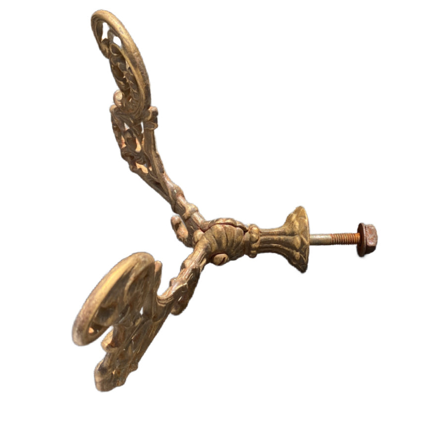 Antique French architectural hardware double hook with symmetrical floral scrolls and a warm metallic gold-gilded surface.