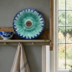 Antique English majolica sunflower plate styled on a shelf in a light filled room with flow blue bowl and french linen