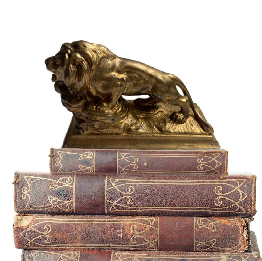 gilded metal lion presse papier with rich patina and elegant detail. A classic French desk accessory adding charm and sophistication to any décor. on a stack of antique leather books