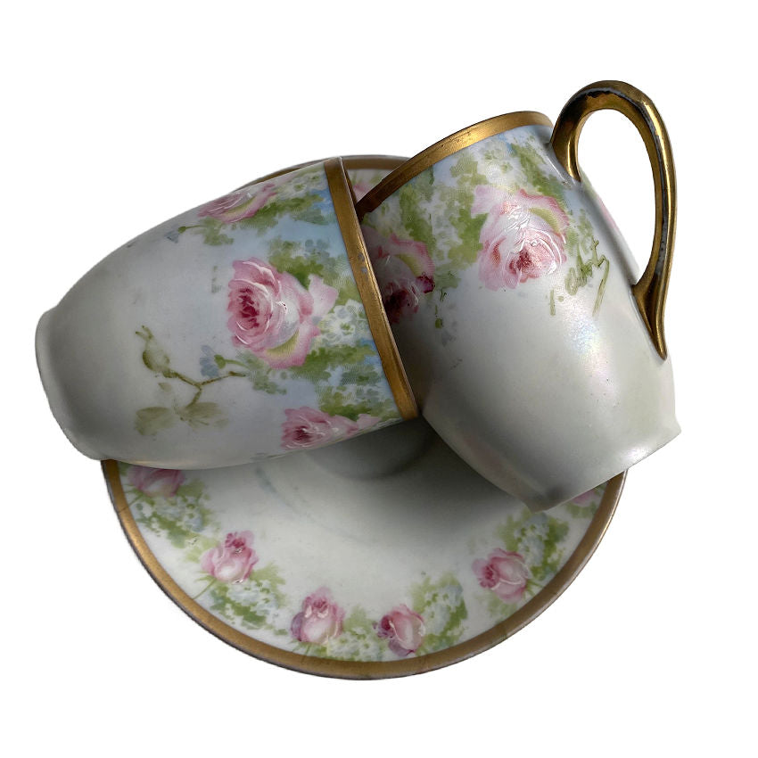 A hand-painted porcelain chocolate pot with pink roses and a lid, accompanied by five cups with the same floral design, all with gold edging.