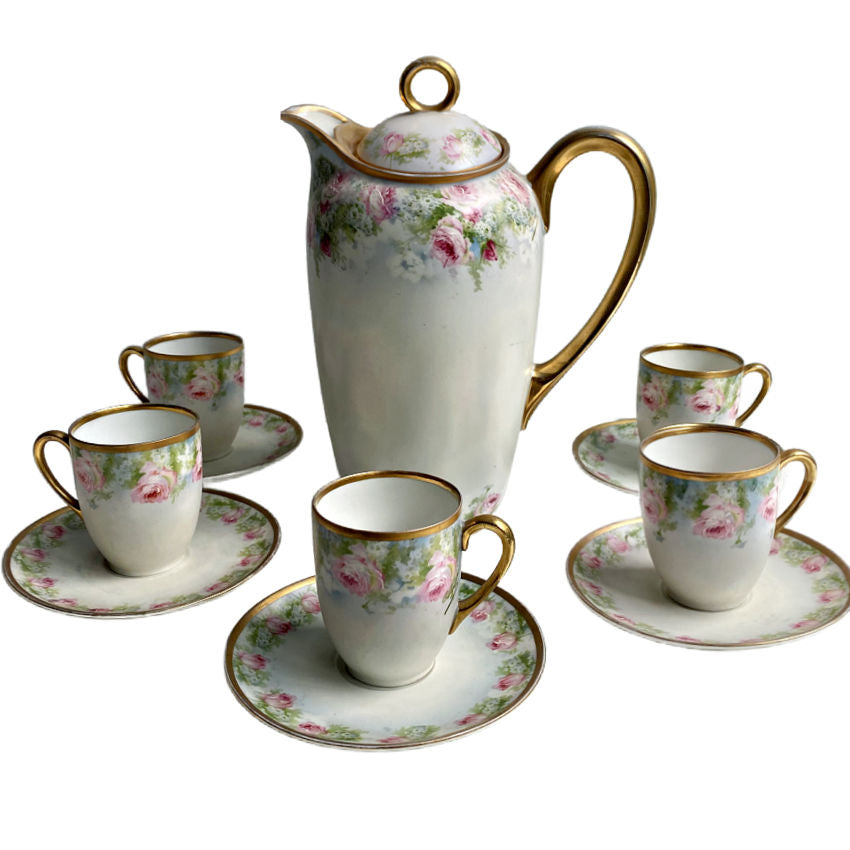 A hand-painted porcelain chocolate pot with pink roses and a lid, accompanied by five cups with the same floral design, all with gold edging.