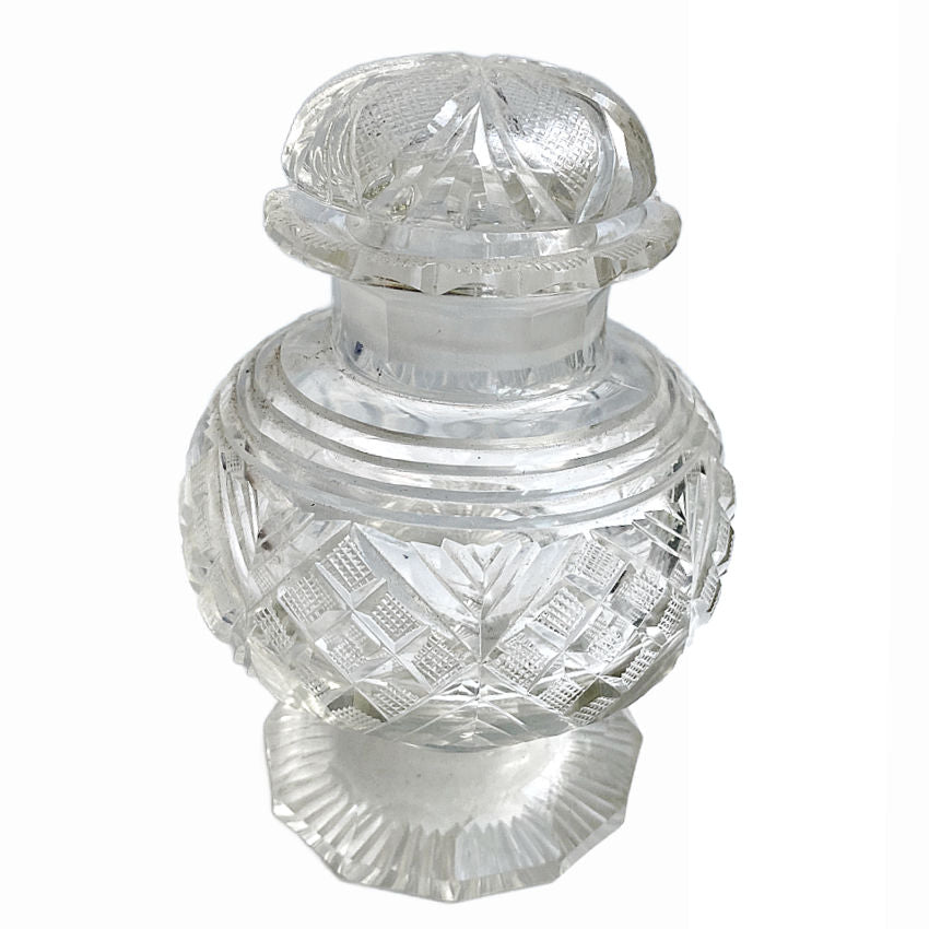 Antique cut glass jar with a scalloped rim, round cut top, and a faceted foot. It features intricate cut patterns and a domed lid with a flower design on top.