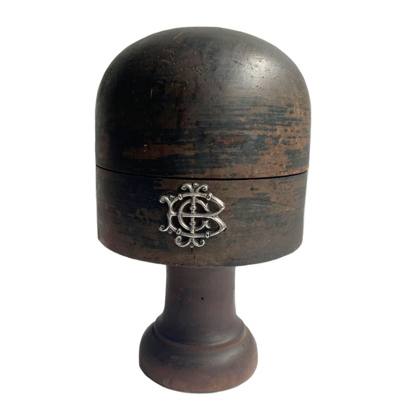 Antique French wooden hat block stand with a silver monogram on the front, displaying signs of aging and use.