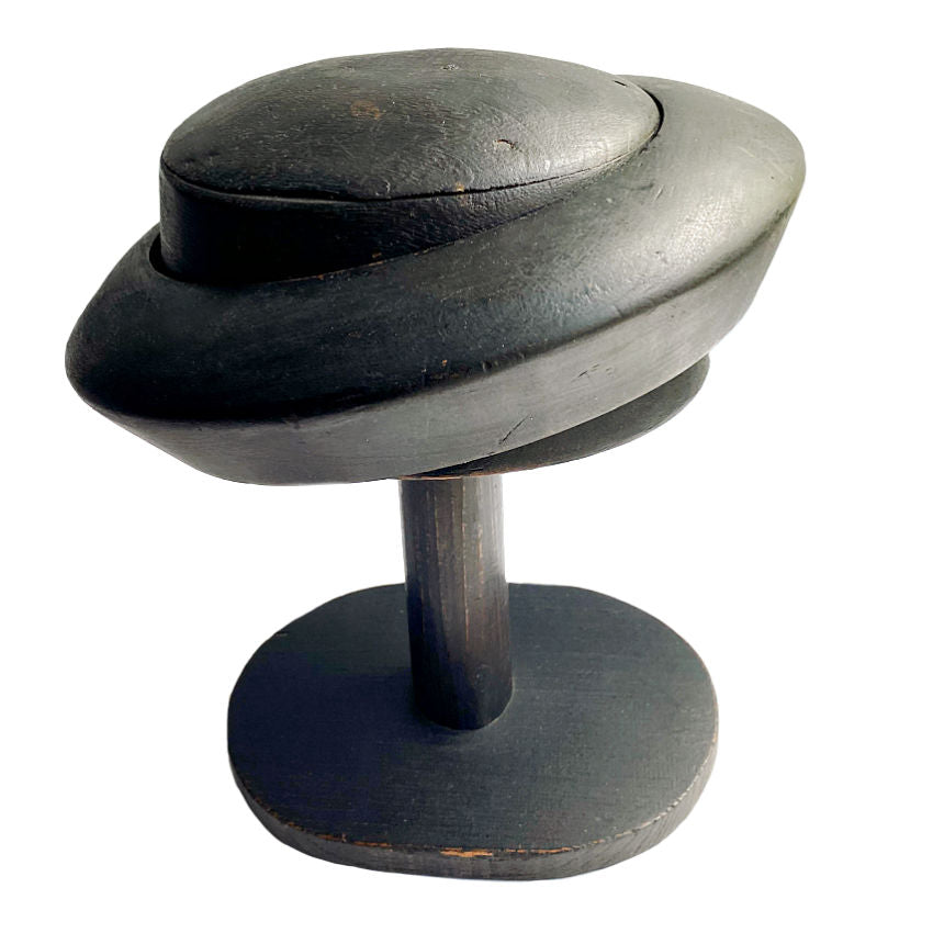 A French 19th Century millinery shop wood hat block stand with a dark patina, featuring a rounded hat form sitting atop a three-piece stand.