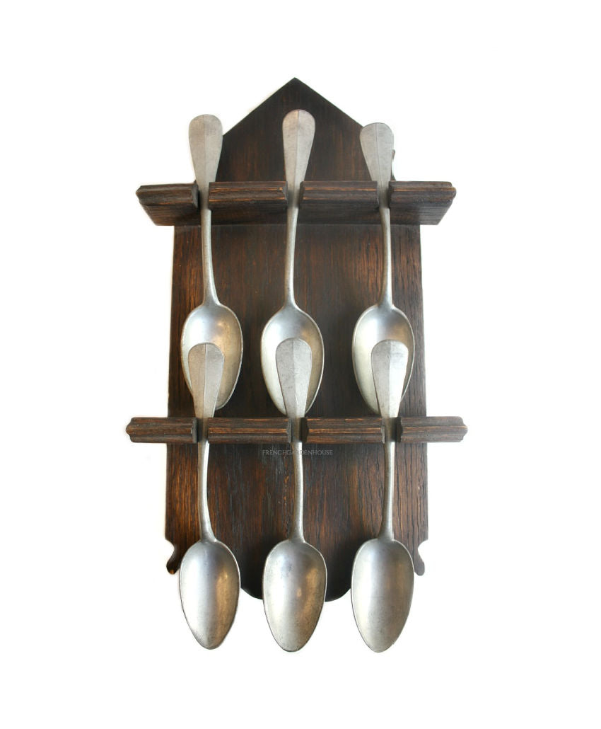 A set of six silver pewter spoons displayed in a French Country rustic antique oak wood rack.