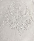 Close-up of white Appenzellembroidered hand towel with a portrait and floral design, showing detailed flower patterns and a monogram.