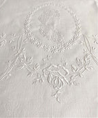Close-up of white Appenzellembroidered hand towel with a portrait and floral design, showing detailed flower patterns and a monogram.
