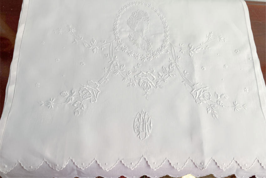Close-up of white Appenzellembroidered hand towel with a portrait and floral design, showing detailed flower patterns and a monogram.