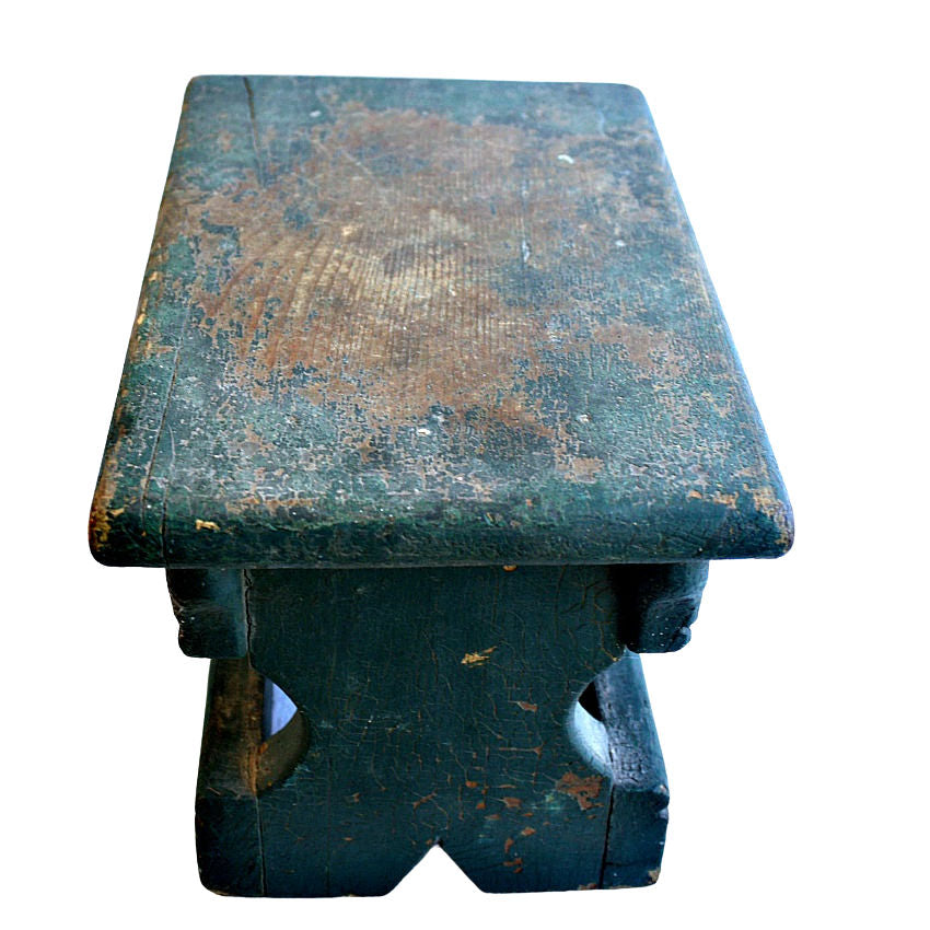 Antique cricket stool with original green paint showing signs of wear and patina, with a wooden structure and apron on the sides.
