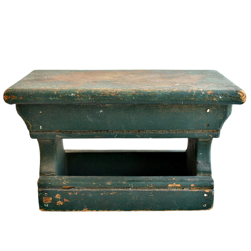 Antique cricket stool with original green paint showing signs of wear and patina, with a wooden structure and apron on the sides.