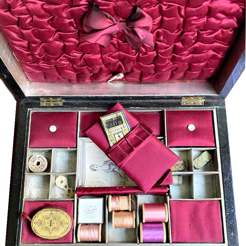 Silk lined compartments containing antique threads, buttons, and needlework tools
