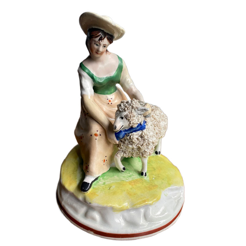 Antique Staffordshire Sheep Shearing Figure, featuring a shepherdess in a green dress and a blue hat, holding a sheep on a yellow and green base.