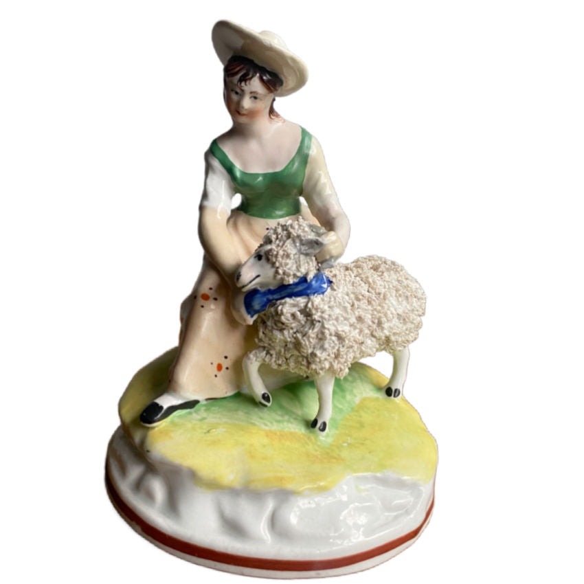Antique Staffordshire Sheep Shearing Figure, featuring a shepherdess in a green dress and a blue hat, holding a sheep on a yellow and green base.