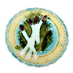 A 19th Century French Majolica Asparagus Plate with a creamy yellow basket weave design, edged by a scalloped turquoise rim, featuring four purple-tipped asparagus on a bed of green leaves against a turquoise ground.