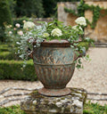 Antique cast iron garden urn with aged verdigris patina and white hydrangea on mossy pillar