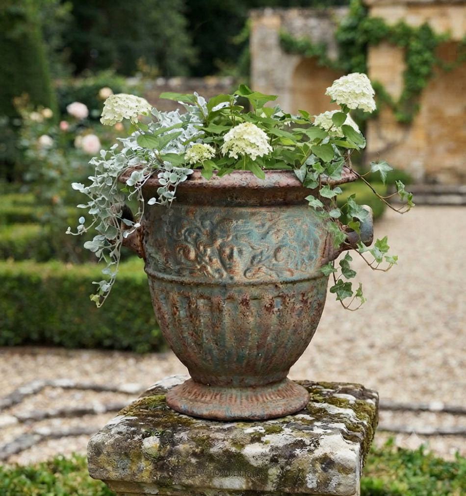 Antique cast iron garden urn with aged verdigris patina and white hydrangea on mossy pillar