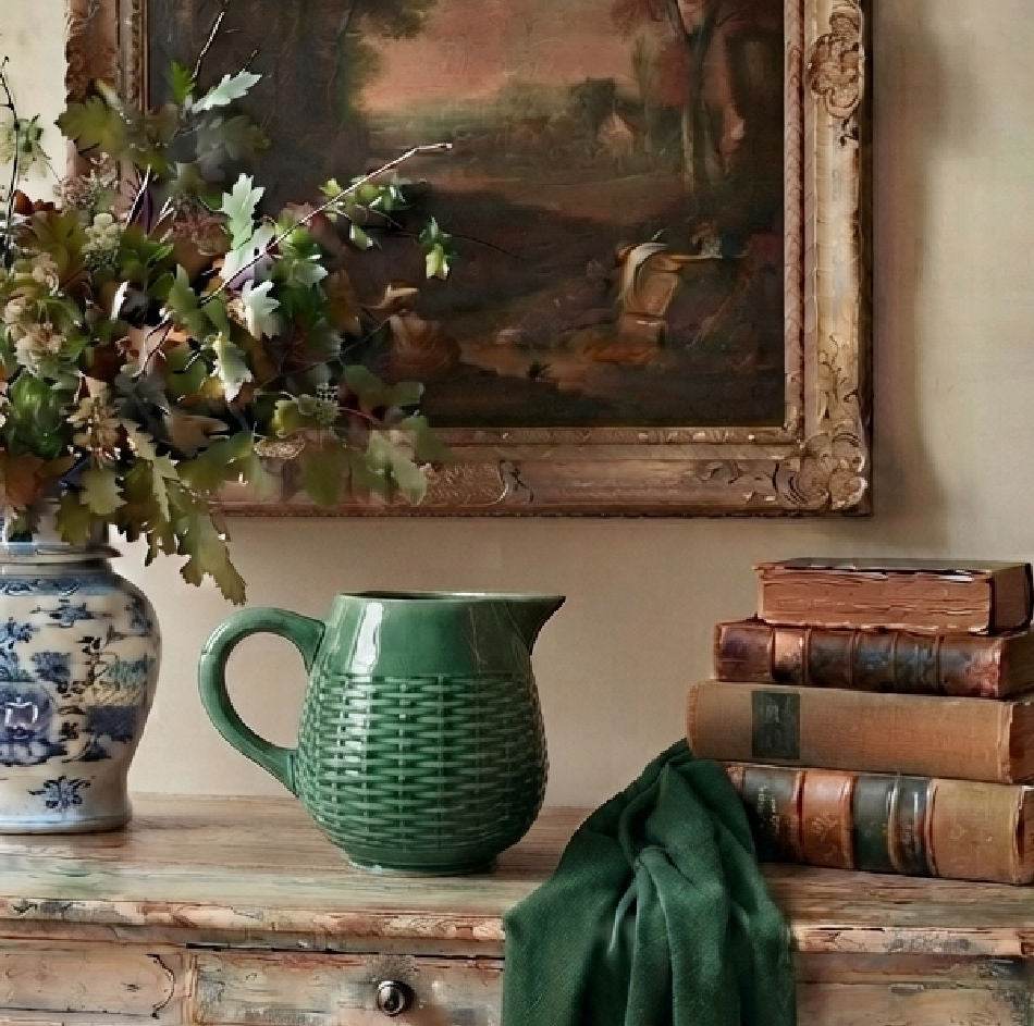 Antique French green majolica basketweave pitcher with glossy green glaze on French country table with books and oil painting