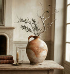 antique French stoneware oil jug styled on a French table with branches, old books, candlelight, and stone fireplace mantel background