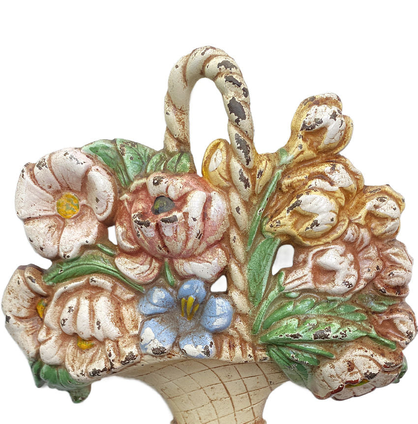 Antique Hubley cast-iron floral basket doorstop with pastel colored flowers and a cream basket with a handle, on a triangular plinth base.