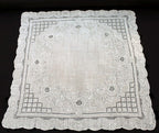 An antique white linen handkerchief with embroidered floral and geometric designs, scalloped edges, and a small border.