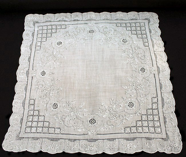 An antique white linen handkerchief with embroidered floral and geometric designs, scalloped edges, and a small border.