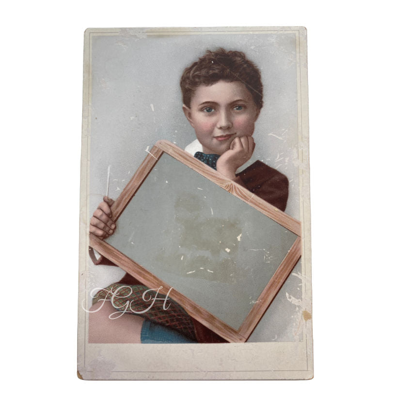 A charming and rare large 19th-century advertising “blank” trade card, featuring a handsome young schoolboy holding an empty slate ready for custom printing or shop branding.