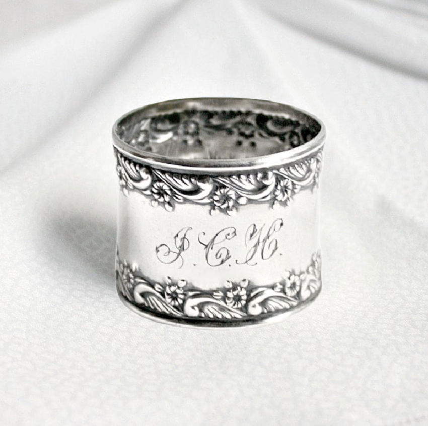 Silver ornate napkin ring with engraved text on a white background