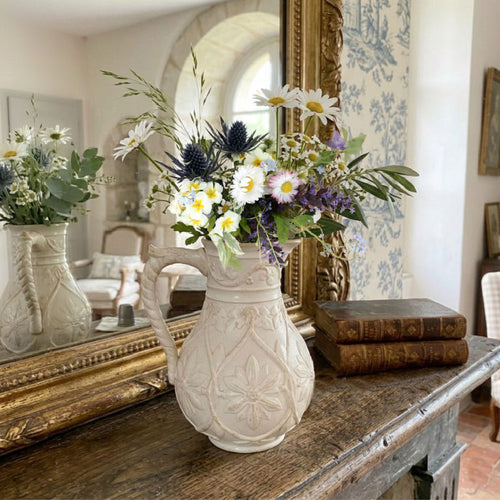 Antique English Gothic Revival stoneware pitcher displayed on rustic wood mantel with fresh flowers in French country living room setting warm natural light decor
