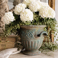 Aged cast iron urn with sculptural faces, verdigris patina, hydrangea, and ivy