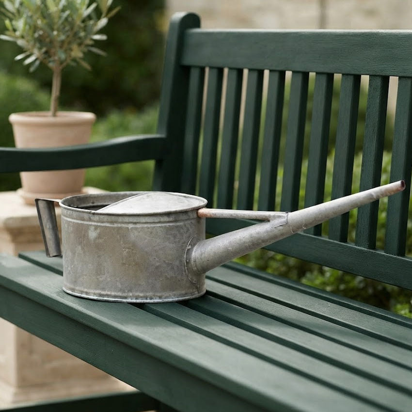 Large vintage-style antique watering can for a country garden on a French green garden bench