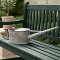 Large vintage-style antique watering can for a country garden on a French green garden bench