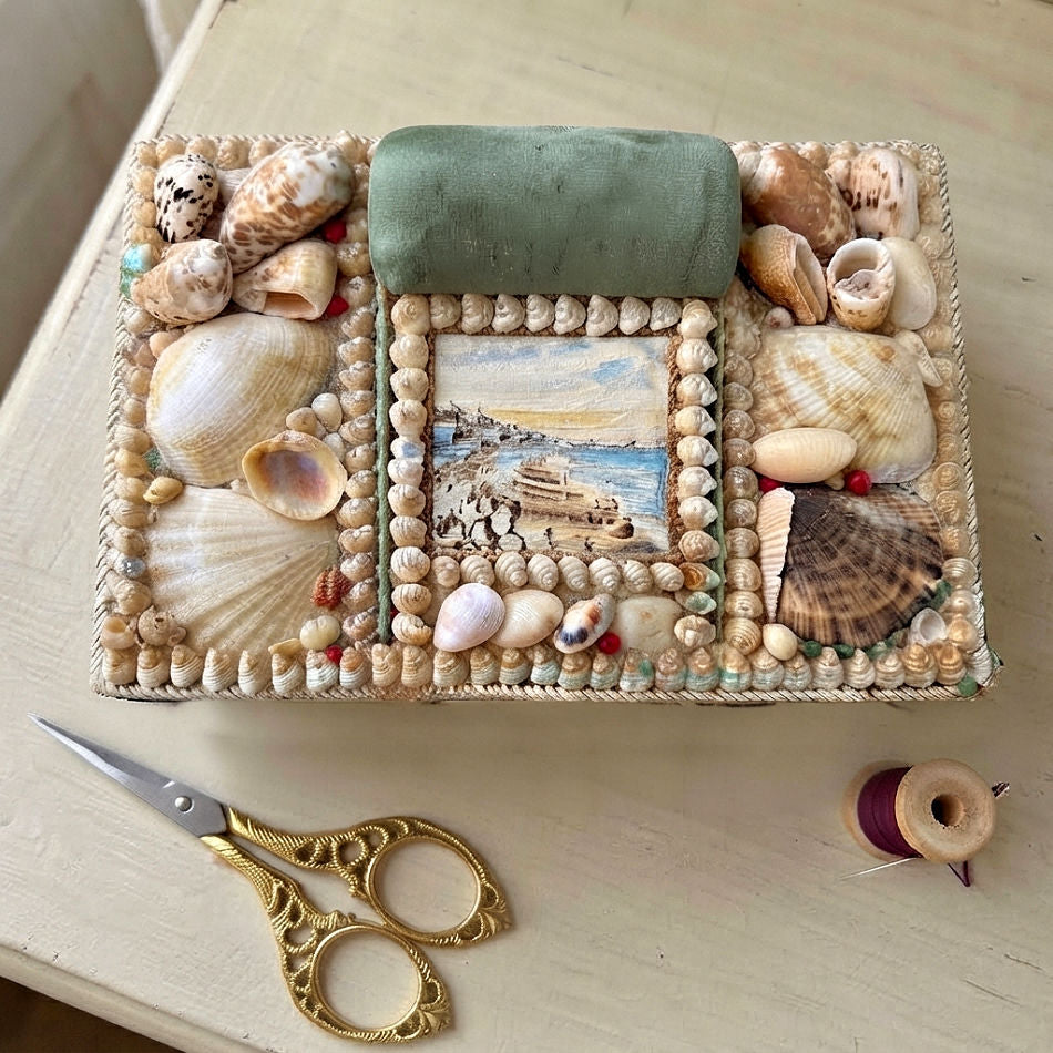 Antique English shellwork sewing box with green silk pincushion with gold scissorson a French cream desk