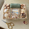 Antique English shellwork sewing box with green silk pincushion with gold scissorson a French cream desk