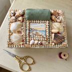 Antique English shellwork sewing box with green silk pincushion with gold scissorson a French cream desk