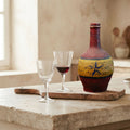 Antique French hand-painted Provençal stoneware wine bottle on an antique french cutting board with two wine glasses