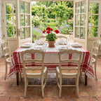 Antique French red and white rose damask tablecloth dressing a farmhouse table in a sun-filled French country sunroom with open French doors overlooking a blooming garden