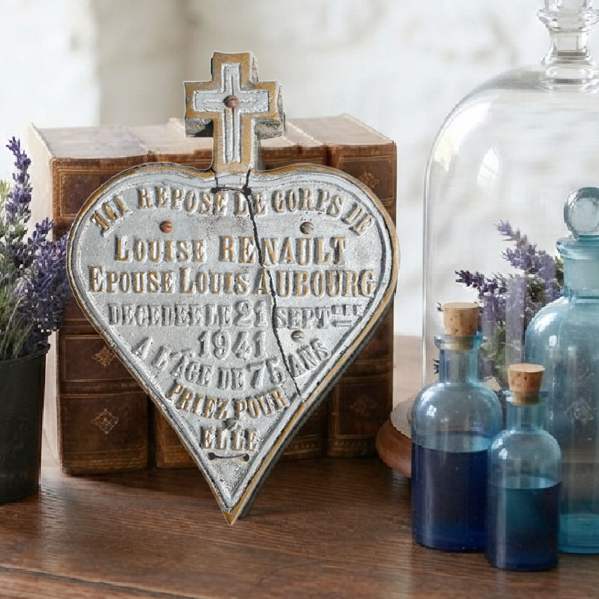 Antique French cemetery memorial plaque displayed on an antique wood desk with aqua glass bottles and leather books